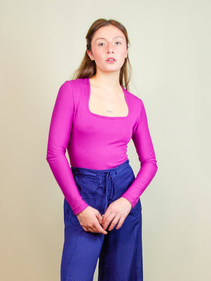 Wearing a long-sleeve bodysuit made from jersey deadstock fabric, featuring a square neckline and a sleek, fitted design. Styled as part of a colorful, slow fashion, made-to-order collection